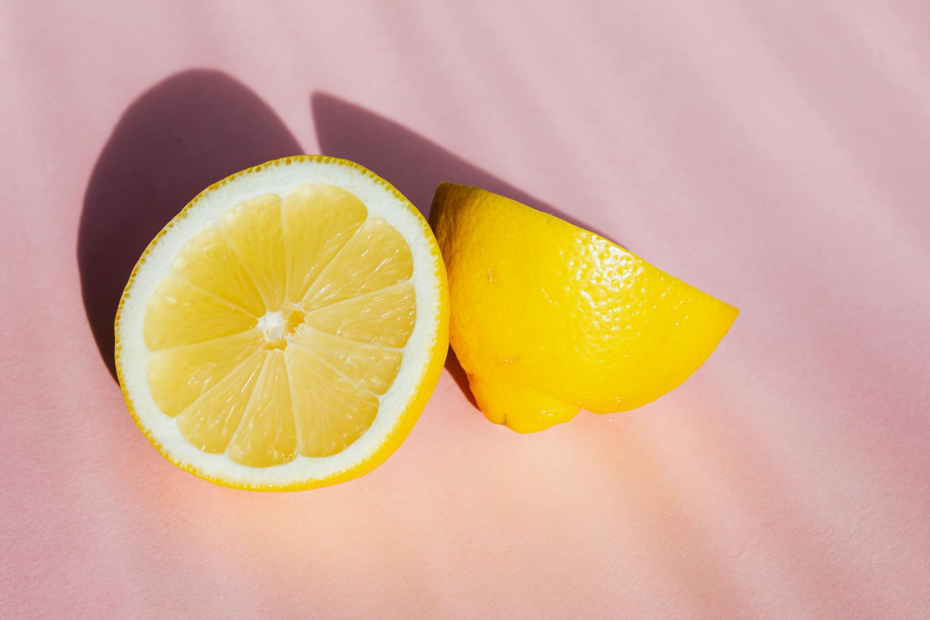 Fresh lemon halves on a pink background in sunlight