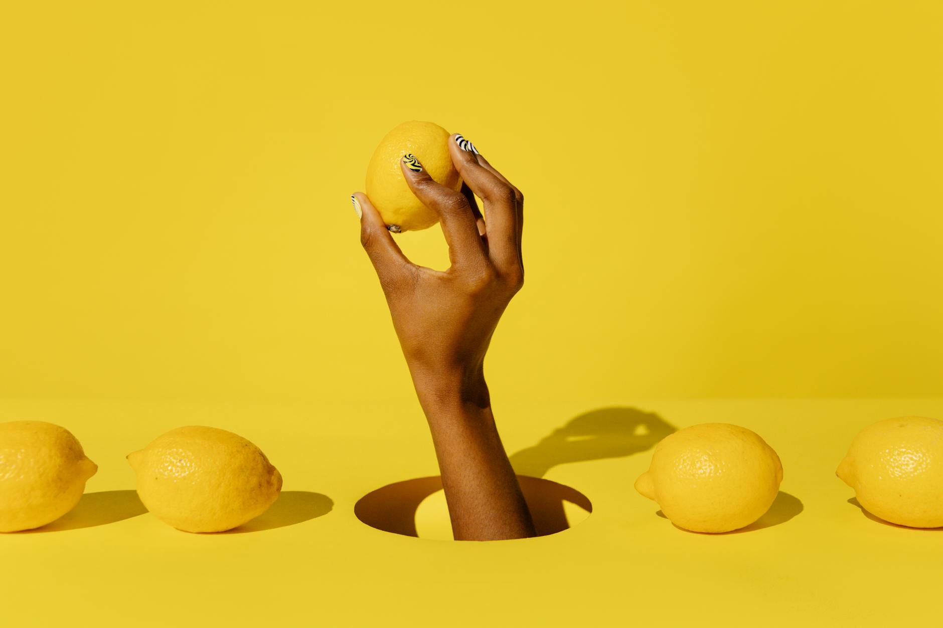 A hand holding a fresh lemon against a bright yellow background, symbolizing renewed sensation and vitality