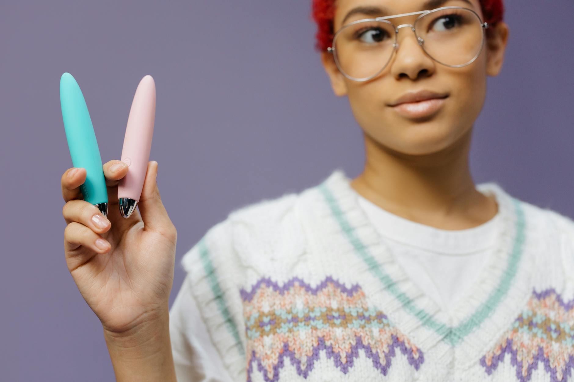 Woman holding two colorful silicone vibrators against a purple background